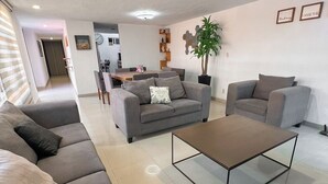 Ein modernes Wohnzimmer mit einem Ecksofa, einem Couchtisch und einer Essgelegenheit im Hintergrund.