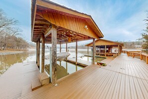 En træterrasse med et overdækket område, en pool og udsigt til en sø.