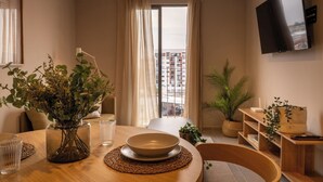 Ein modernes Wohnzimmer mit Essbereich, einem wandmontierten Flachbildfernseher und Blick auf ein Gebäude durch das Fenster.