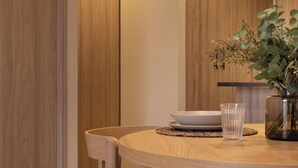 Ein Essbereich mit einem runden Holztisch, Stühlen und einer Vase mit getrockneten Blumen.