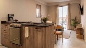 Eine moderne Küche mit Einbauherd, Kaffeemaschine und Spüle. Es gibt einen Essbereich mit einem Stuhl und Tisch. Ein Fernseher ist an der Wand montiert.
