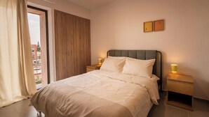 Ein Schlafzimmer mit einem Bett, Nachttischen, einem Fenster mit Vorhängen und Blick auf Gebäude.