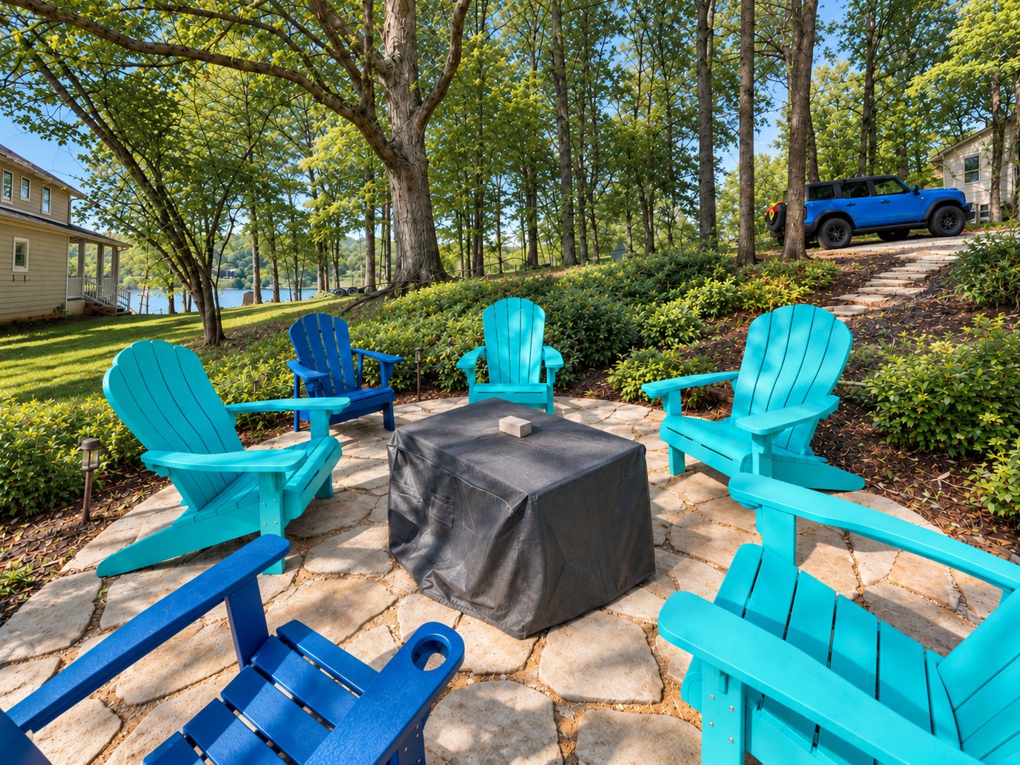 An outdoor seating area with Adirondack chairs and a table, surrounded by stone paving and greenery.