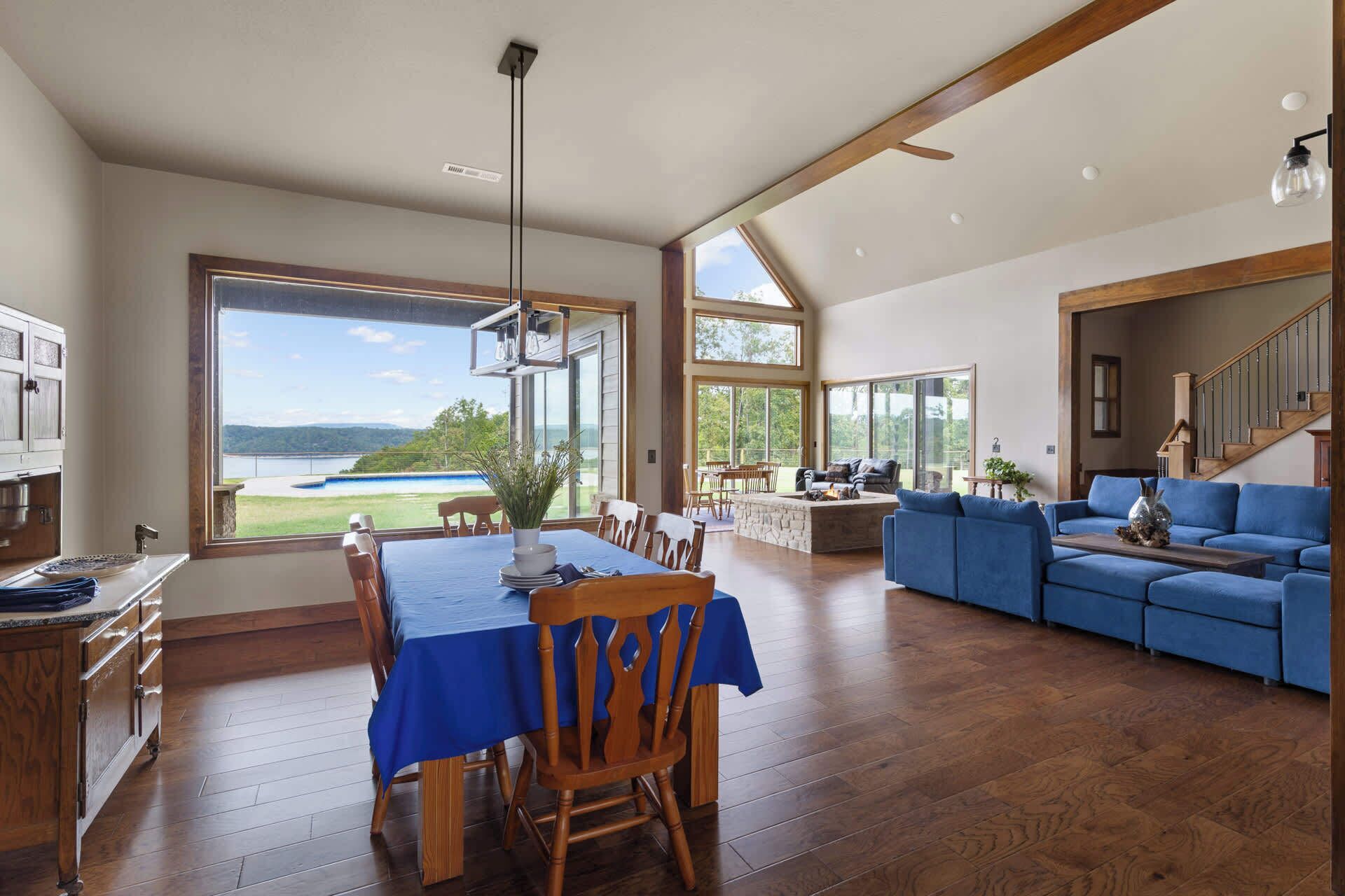 A spacious living room with a large dining table, blue sofa, and a view of a lake.