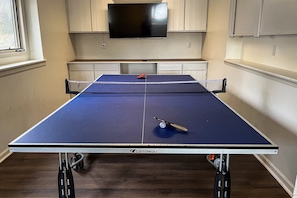 A ping pong table with a TV above it, wooden cabinets, and a window. - LakeDaze - Dog-friendly, Lakefront, Dock, Hot Tub, Putting Green, Game Room (Moneta)