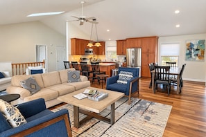 A modern living room with a sofa, armchair, and coffee table, a dining area with a table and chairs, and a kitchen with wooden cabinets and appliances. - LakeDaze - Dog-friendly, Lakefront, Dock, Hot Tub, Putting Green, Game Room (Moneta)