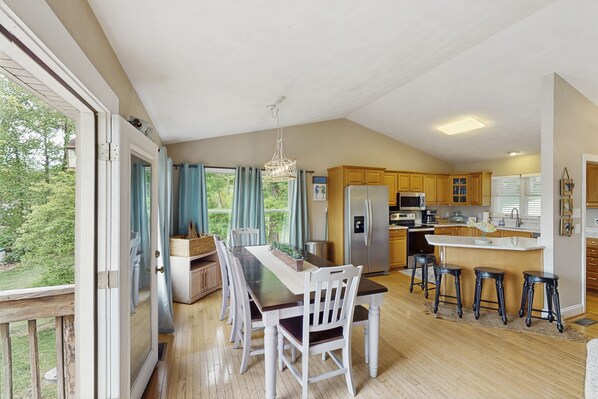 A spacious kitchen with wooden cabinets, a central island with stools, and a large window overlooking a garden. - Wet Feet Retreat - Lakefront with incredible views, dock, pool table, foosball (Moneta)