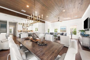 A spacious living area with a wooden ceiling, a dining table, and a modern kitchen in the background. - 392 Walton Rose - Access to Rosemary Beach Fitness, Tennis, 4 Adult bikes! (Inlet Beach)