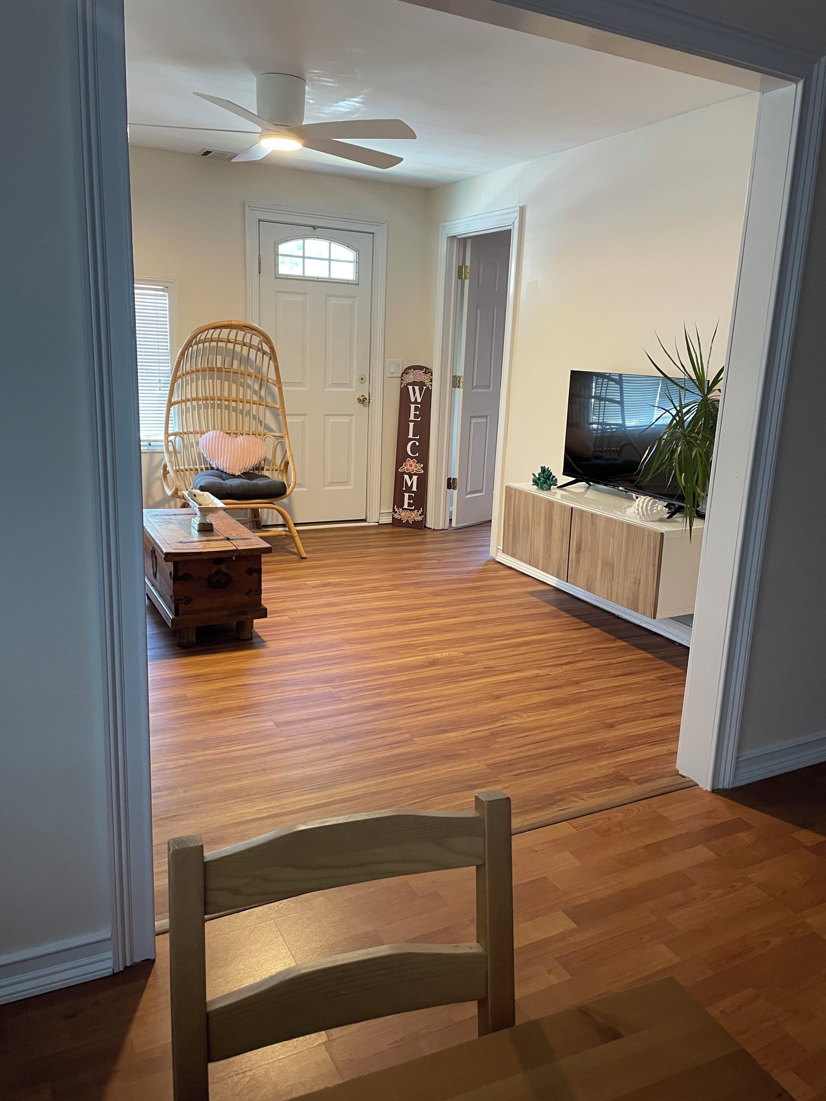 A room with a wooden floor, a wicker chair, a television, and a welcome sign.