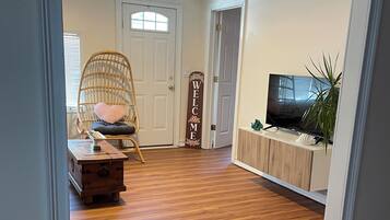 A room with a wooden floor, a wicker chair, a television, and a welcome sign.