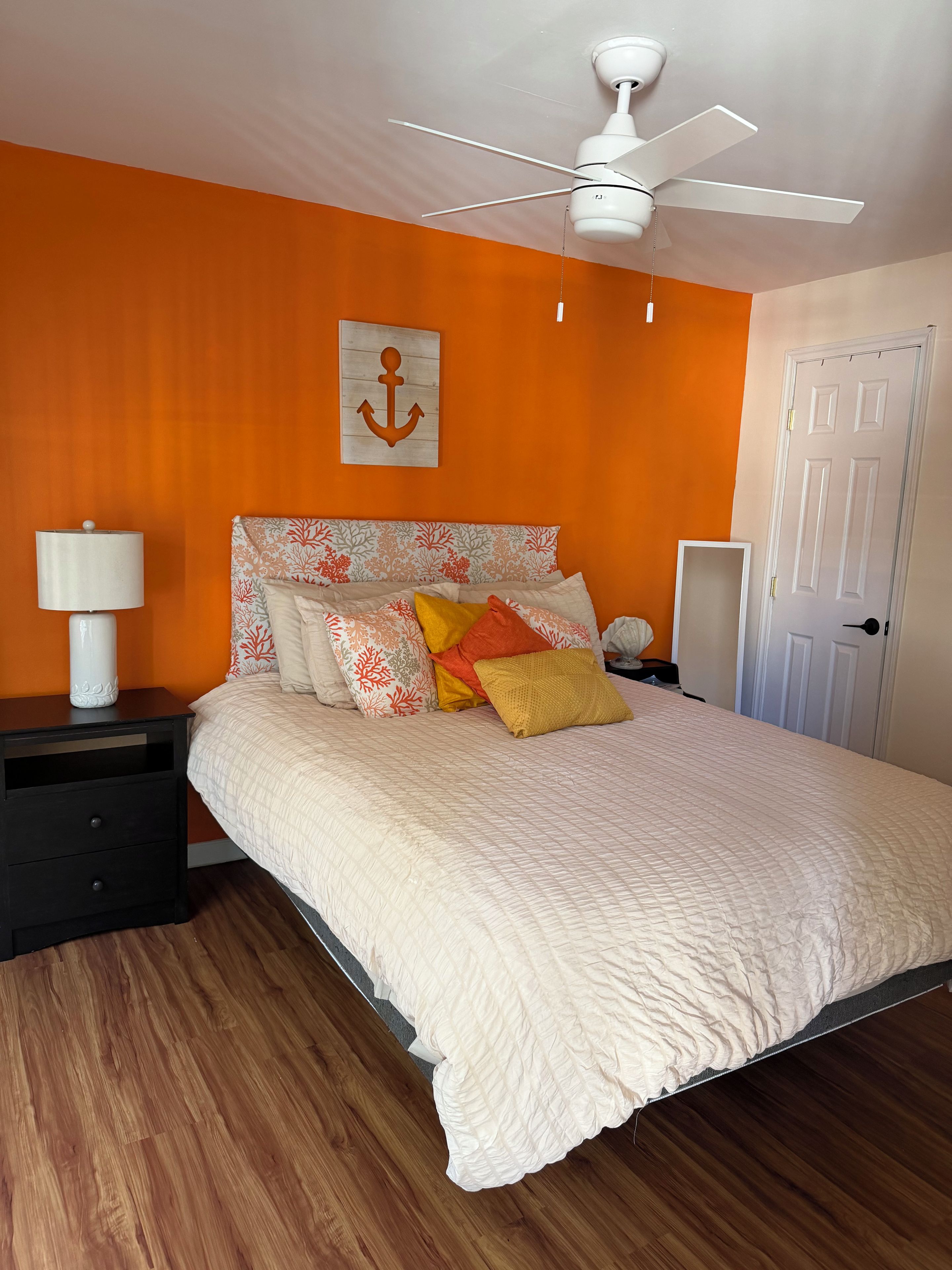 Un dormitorio con cama, mesitas de noche, ventilador de techo y una obra de arte con forma de ancla en la pared.