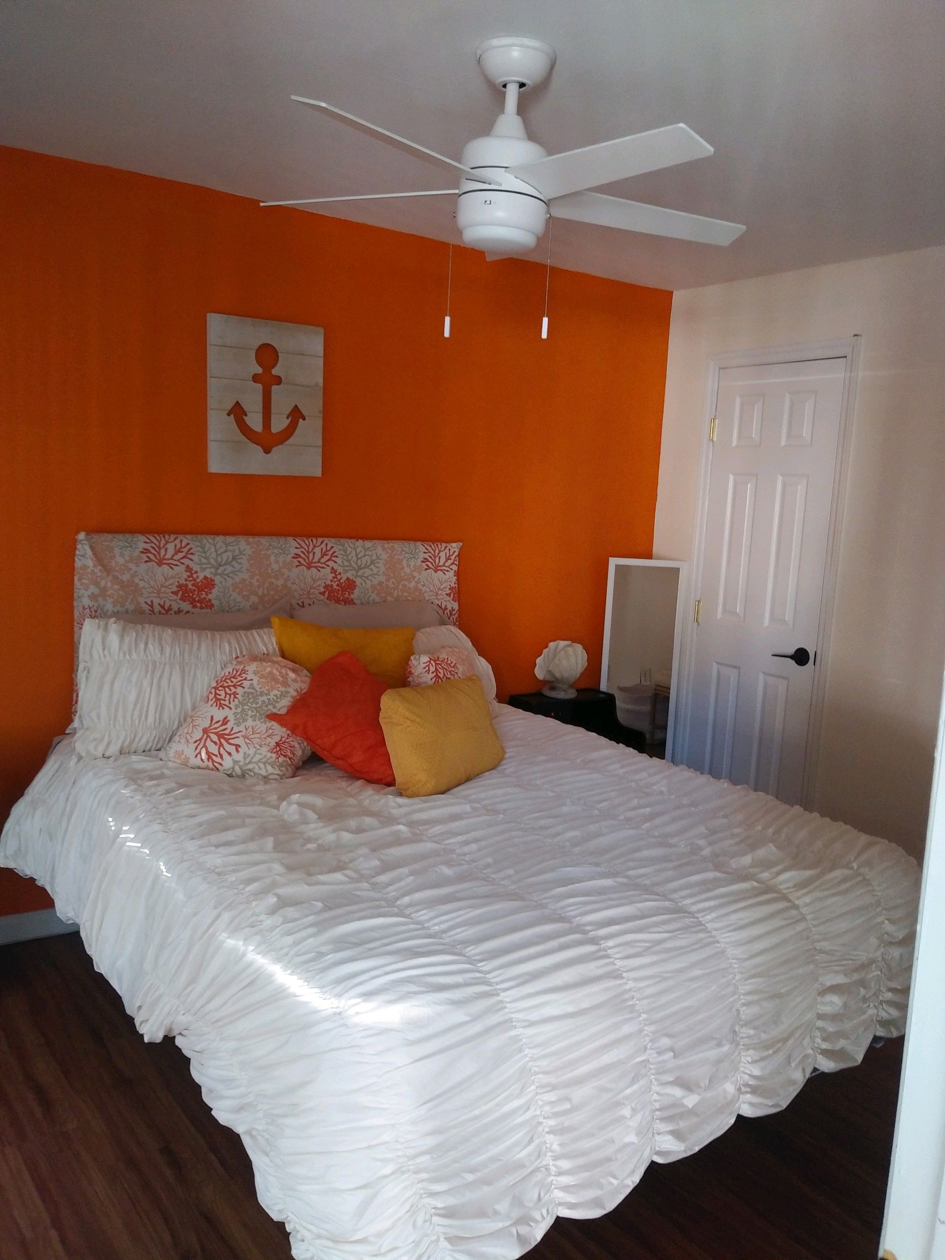 A bedroom with a bed, a ceiling fan, an anchor decoration, and a door.