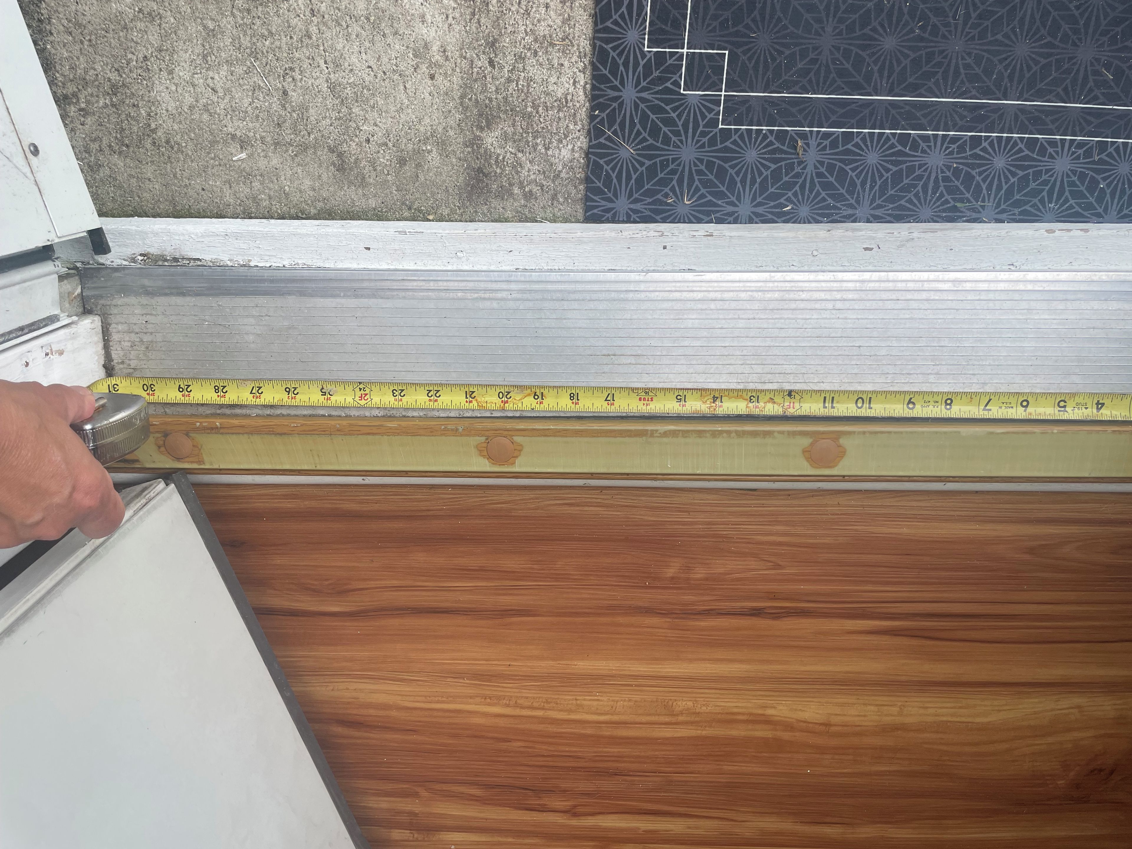Une main mesure une surface en bois à l’aide d’un mètre ruban jaune.