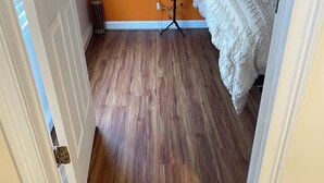Ein Flur mit Holzboden, einem Bett mit weißer Bettwäsche und einem kleinen Tisch mit einer Lampe.