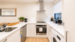 A modern kitchen with a stainless steel range hood, a built-in oven, a dishwasher, and a washing machine. - Salisbury Garden | 2BR with Parking | CBD (Christchurch)
