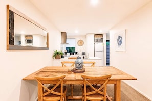A dining area with a wooden table and chairs, a large mirror, a clock, and a kitchen in the background. - Salisbury Garden | 2BR with Parking | CBD (Christchurch)