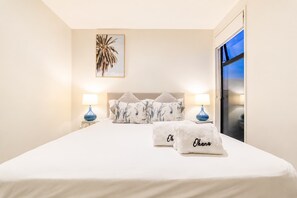 Une chambre d’hôtel avec un lit, deux lampes de chevet, une grande fenêtre et un tableau encadré au mur.