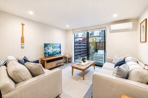 A modern living room with a flat-screen TV, two sofas, a coffee table, and a sliding glass door leading to a balcony. - Salisbury Garden | 2BR with Parking | CBD (Christchurch)