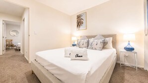 A hotel room with a large bed, two bedside lamps, a bedside table, and a wall-mounted artwork. - Salisbury Garden | 2BR with Parking | CBD (Christchurch)