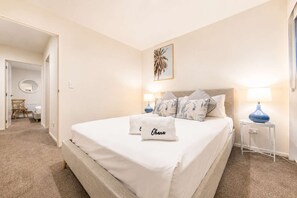 Ein Hotelzimmer mit einem großen Bett, zwei Nachttischlampen, einem Nachttisch und einem an der Wand befestigten Kunstwerk.