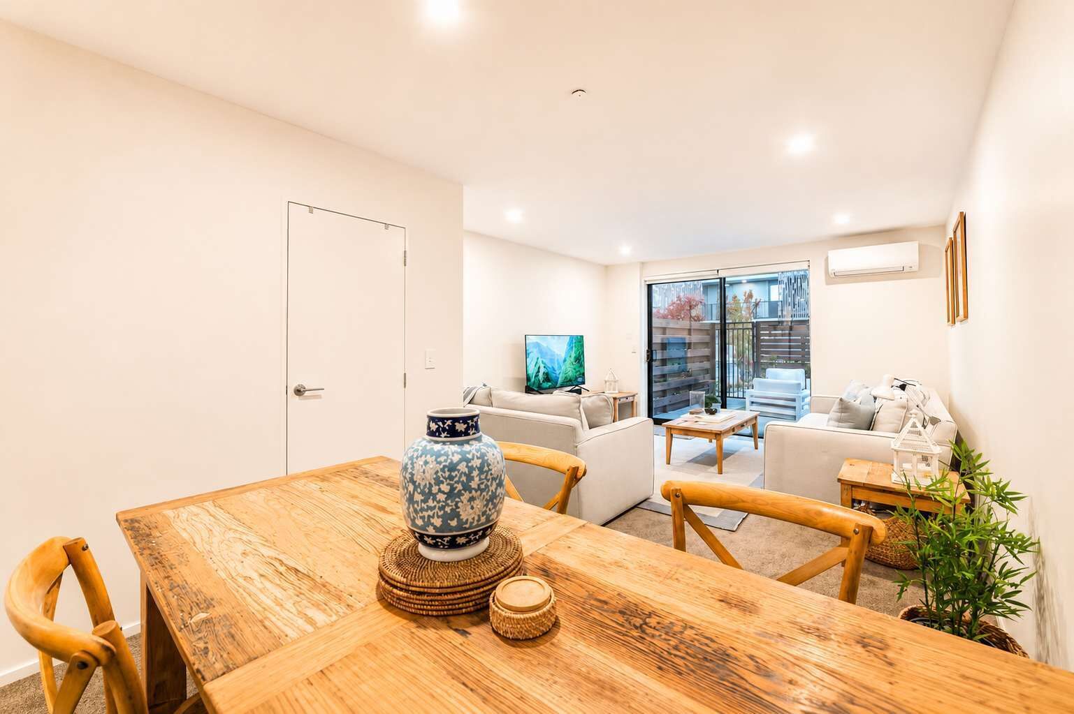 A dining area with a wooden table, chairs, a decorative vase, and a television in the background.