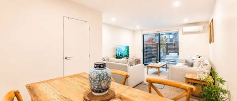 A dining area with a wooden table, chairs, a decorative vase, and a television in the background.
