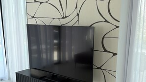 Ett modernt vardagsrum med en stor tv-skärm på ett svart tv-bord, en vägg med mönster och ett vitt golv.