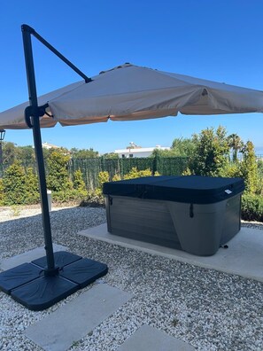 A patio with a table and an umbrella, gravel ground, and a view of a building and trees. - Villa Sotogrande- Sleeps 10 - Pool Access- jacuzzi (San Roque)