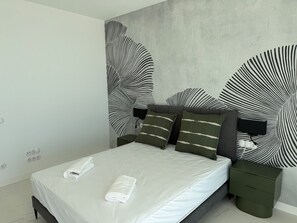 A modern bedroom with a bed, pillows, a nightstand, and a wall with a leaf pattern. - Villa Sotogrande- Sleeps 10 - Pool Access- jacuzzi (San Roque)