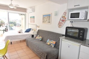 Ein Zimmer mit einem Bett, einem grauen Sofa, einer kleinen Küchenzeile mit einer Mikrowelle, einem Toaster und einem Fenster mit Blick auf die Stadt.
