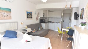 A hotel room with a bed, a sofa, a dining table with chairs, a kitchen area, and a ceiling fan. - Discover this charming studio located in Santa Margarita, Roses! (Roses)