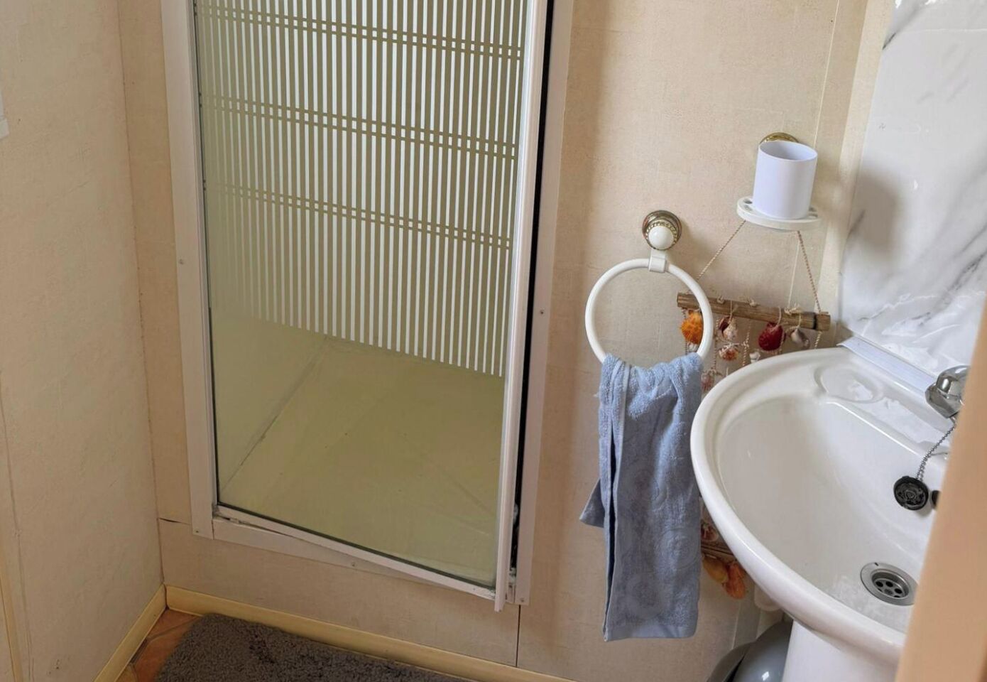 Un baño con mampara de vidrio, lavamanos y un perchero para toallas.