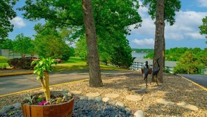 A landscaped area with trees, a pond, and a bird sculpture. - Cozy Lakefront Condo w/ 10x24 Slip & Fishing (Osage Beach)
