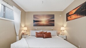 A bedroom with a large bed, two bedside tables with lamps, a painting on the wall, and a window with curtains. - Cozy Lakefront Condo w/ 10x24 Slip & Fishing (Osage Beach)