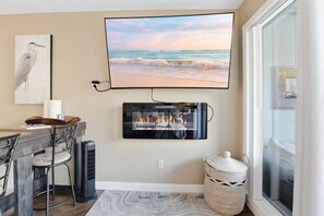 A room with a TV mounted on the wall, a fireplace below it, a dining table with chairs, and a large window. - Cozy Lakefront Condo w/ 10x24 Slip & Fishing (Osage Beach)