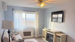 Ein Wohnzimmer mit einer Couch, einem Couchtisch, einem Fernseher, einem Deckenventilator und einem Fenster mit Vorhängen.