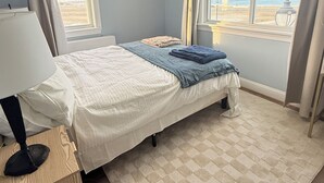 Ein Schlafzimmer mit einem Bett, einem Schreibtisch, einem Deckenventilator und Blick auf den Strand.