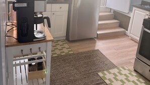 Eine kompakte Küche mit weißen Schränken, einem Edelstahlkühlschrank, einer Kaffeemaschine und einer kleinen Arbeitsfläche.