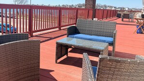 Eine rote Terrasse mit Korbmöbeln, einem Ziegelkamin und Blick aufs Wasser.