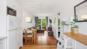 Eine moderne Küche mit Mikrowelle, Essbereich mit Holzsesseln, eine Couch mit Kissen und Blick auf Grünfläche.