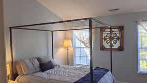 Ein Bett mit Baldachin, ausgestattet mit einer gestreiften Tagesdecke, einer Nachttischlampe und einem kleinen Holzschemel.