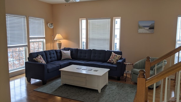 Ein Wohnzimmer mit einem Ecksofa, einem Couchtisch, einer Lampe und einem Gemälde an der Wand.