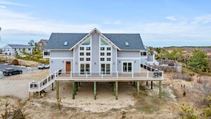 Ein zweistöckiges Haus mit Balkon, Holzterrasse und Strand.