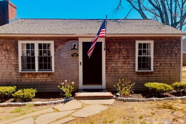Cozy, welcoming Cape Cod style cottage with a stone walkway and beautiful greenery