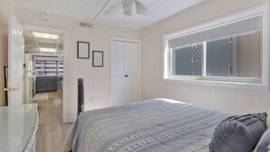 Un dormitorio con cama, ventana con vista, ventilador de techo y puerta que da a otra habitación.