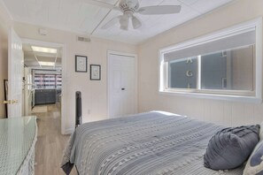 Ein Schlafzimmer mit Bett, Fenster mit Blick, Deckenventilator und einer Tür zu einem anderen Raum.