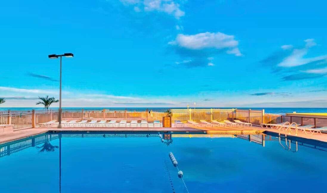 Une piscine offrant une vue dégagée sur le ciel et l’horizon lointain, entourée d’une clôture et de palmiers.