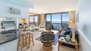 A modern living room with a kitchen, a dining area, and a large window with a view of the ocean. - Golden Sands 1106: Gorgeous Oceanfront 1BR condo | Fully renovated and decorated (Ocean City)