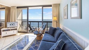 A balcony with a view of the ocean, a sofa, a coffee table, and a sign for Ocean City Vacation Homes. - Golden Sands 1106: Gorgeous Oceanfront 1BR condo | Fully renovated and decorated (Ocean City)