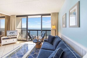 A balcony with a view of the ocean, a sofa, a coffee table, and a sign for Ocean City Vacation Homes. - Golden Sands 1106: Gorgeous Oceanfront 1BR condo | Fully renovated and decorated (Ocean City)